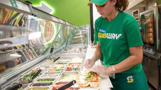 Sandwich Artist making a footlong sub for a customer.