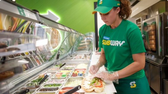 Sandwich Artist making a footlong sub for a customer